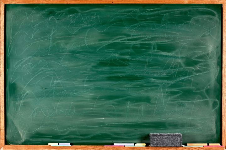 An image of a green chalkboard that has been erased, with chalk and erasers on a shelf below