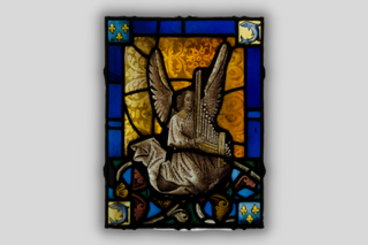 A fragment of a stained glass window in tones of blue and gold depicting an angel robed in white playing a portatif organ.