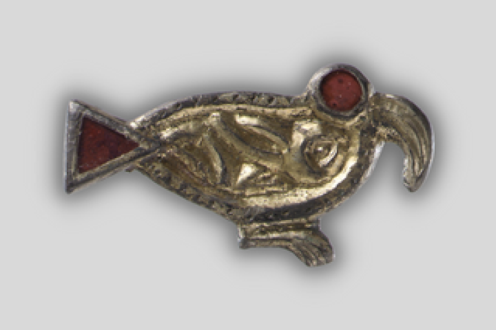 A sixth-century brooch in the shape of a bird seen from the side, with a sharply hooked beak and a large red eye, made of silver-gilt and garnets.