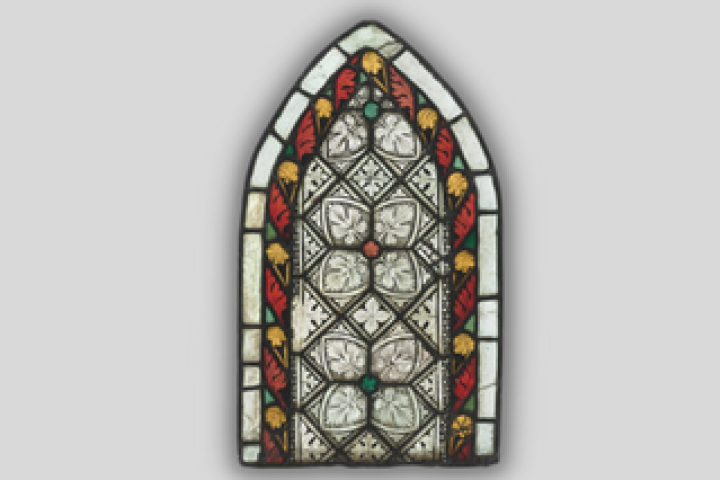 A stained glass window in the shape of a pointed arch, with a red, green, and yellow foliate border and internal panes painted with aconite leaves.