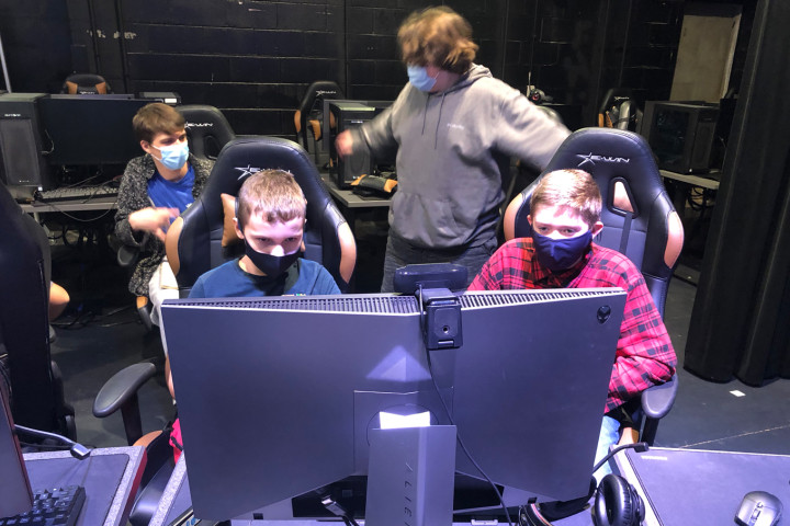 Two kids sitting at gaming terminal with one kid watching behind them play a gaming session