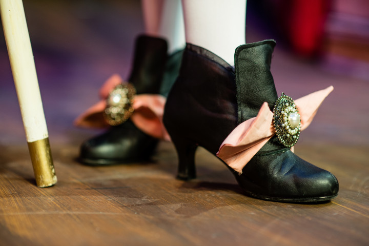 Black period shoes with a pink bow on a wood floor with a cane.