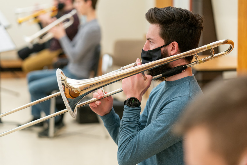A man in a mask blows into a trombone.
