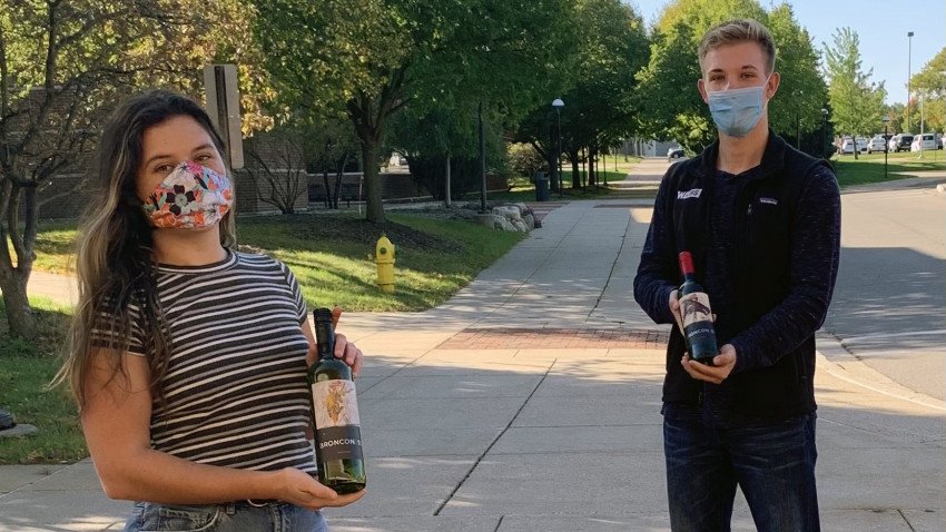 Students socially distanced outdoors wearing masks and holding wine bottles