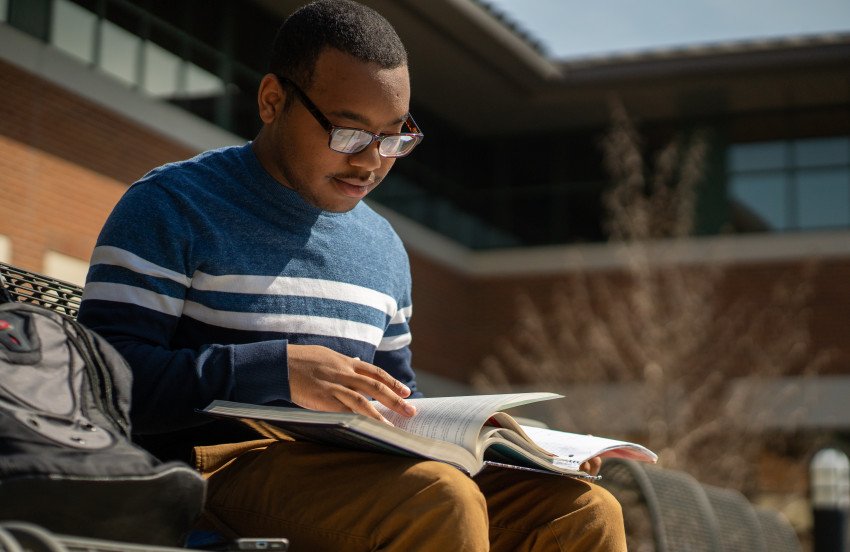 Student sitting outside on a bench looking at an open textbook