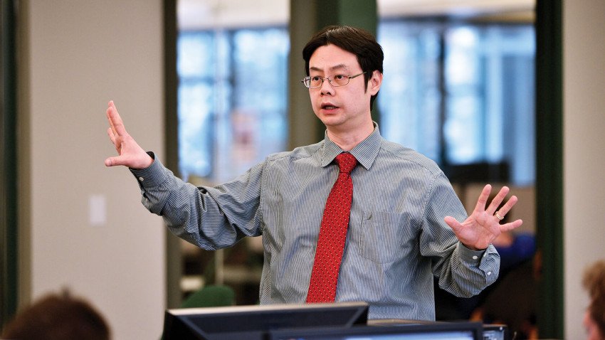 Dr. KC Chen teaching in front of a class with a red tie and button down shirt on