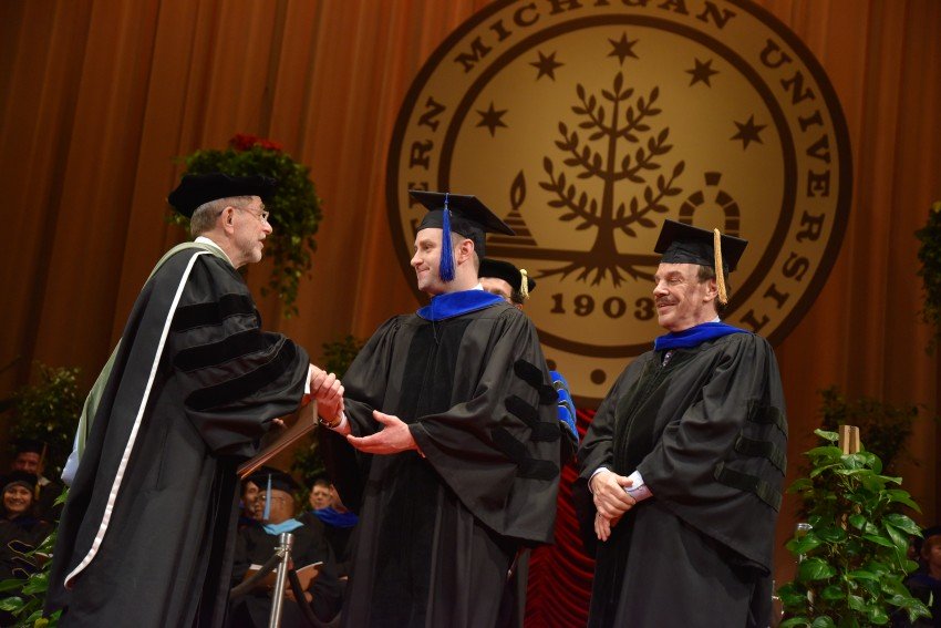 President Dunn shaking hands with a doctoral student on stage at graduation