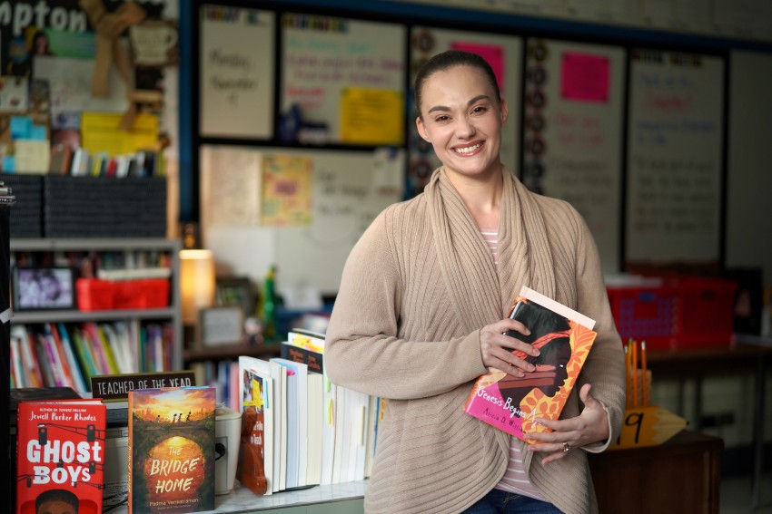 Teacher Stephanie Hampton stands in front of her desk holding a book.