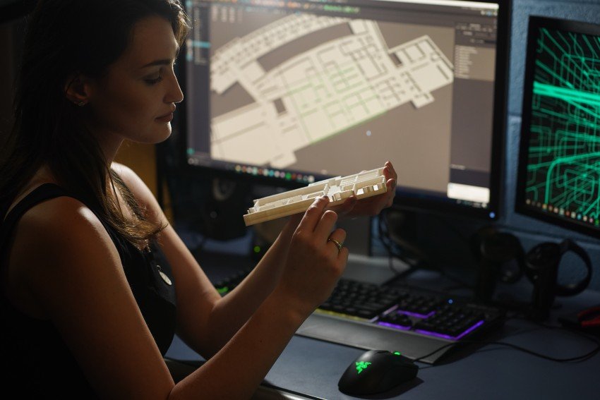 A student holds a 3D map prototype with a larger scale project on the computer screen in the background.