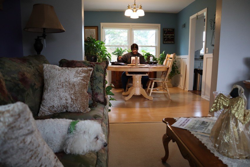 Lucinda Stinson teaches from her dining room table while her dog lays on the couch.