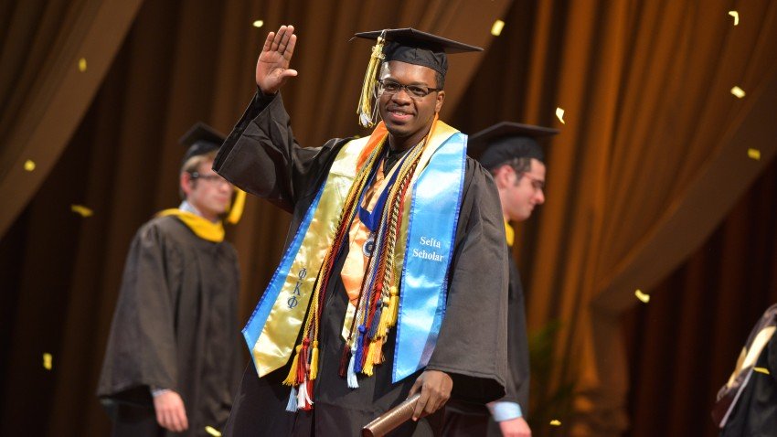 J. Gabriel Ware, dressed in his graduation regalia, waves at the camera after receiving his diploma.