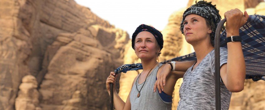Two young women are photographed in the desert looking off into the distance.