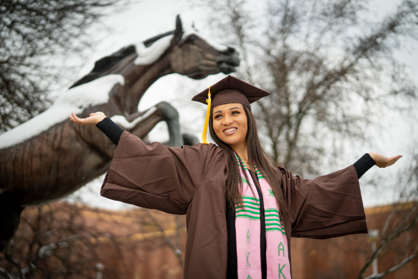 taylor Gaines stainds in front of the Bronco statue in her graduation cap and gown.
