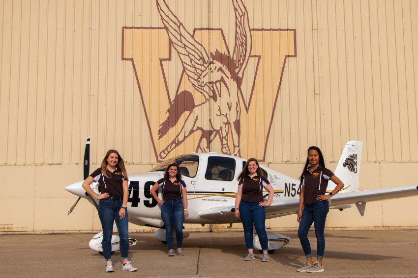 Four aviation students stand in front of their plane.
