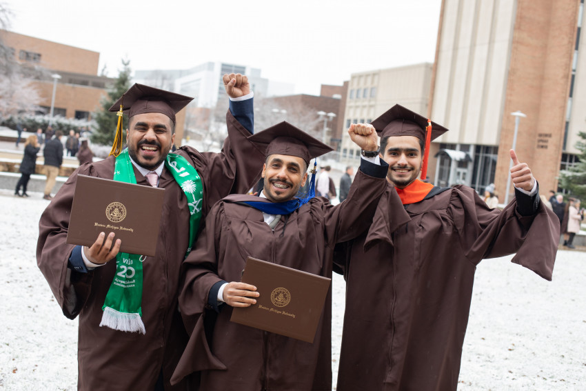 Three WMU alumni show off their diplomas after a commencement ceremony.
