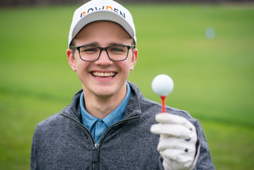 Spencer Rochowiak holds up a golf tee with a ball on it.