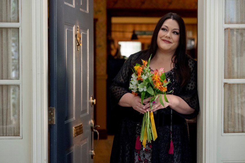 Brooke Elliott stands in a doorway holding a bouquet of flowers. Photo courtesy: Netflix.