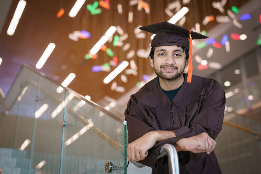 Bharat Goel leans on a railing dressed in his graduation cap and gown.