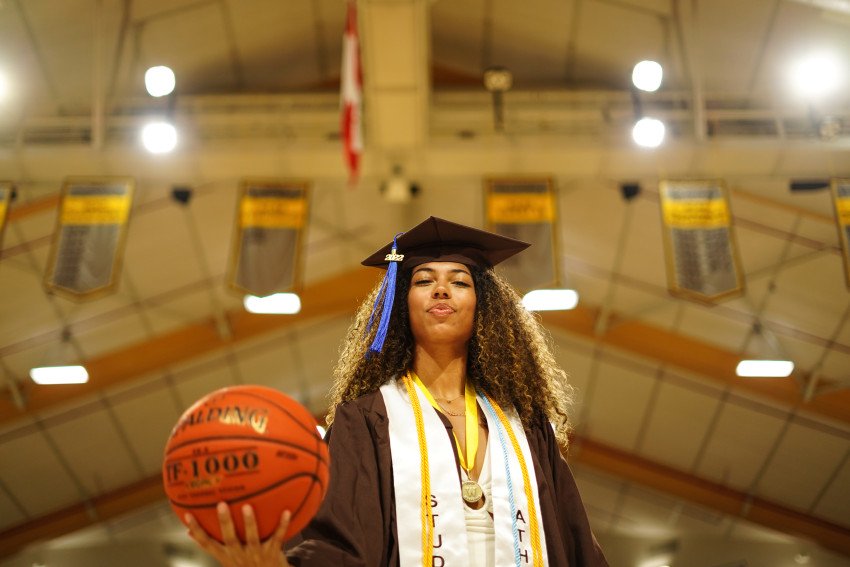 Hannah Douglas holds a basketball while wearing her graduation cap and gown.