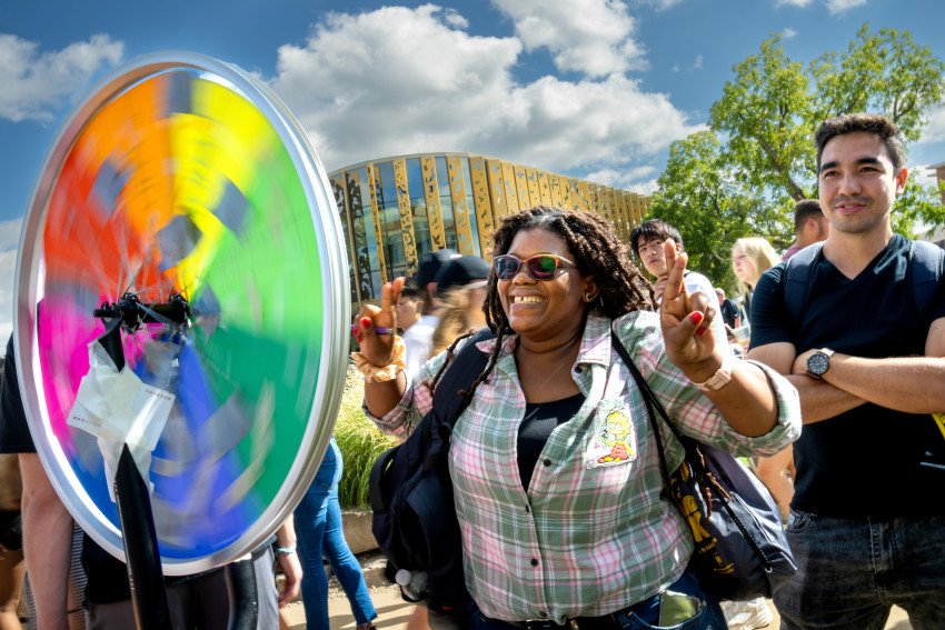 A woman in a button down shirt crosses her fingers as she spins a colorful wheel.