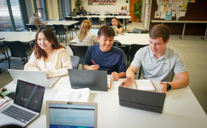 Three students sit at a table on their laptop computers.