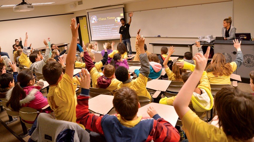 Photo of students raising hands in a classroom.