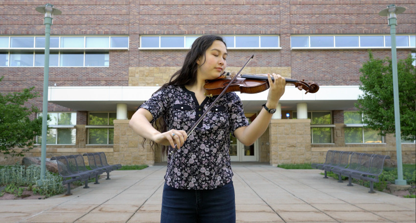A woman plays violin outside of the College of Health and Human Services.