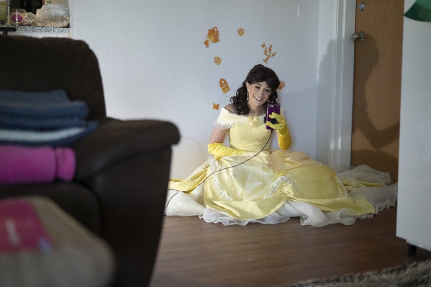 A student dressed as a princess smiles into her phone camera while doing a FaceTime call in her apartment.