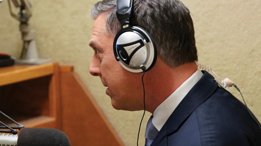 A news anchor standing with headphones on in front of a microphone.