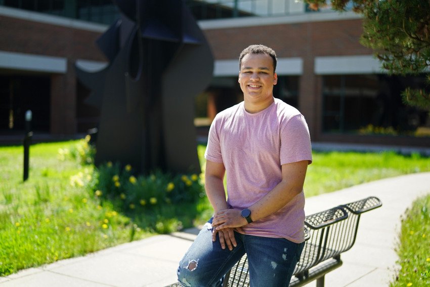 A first year student stands in front of a sculpture on campus.