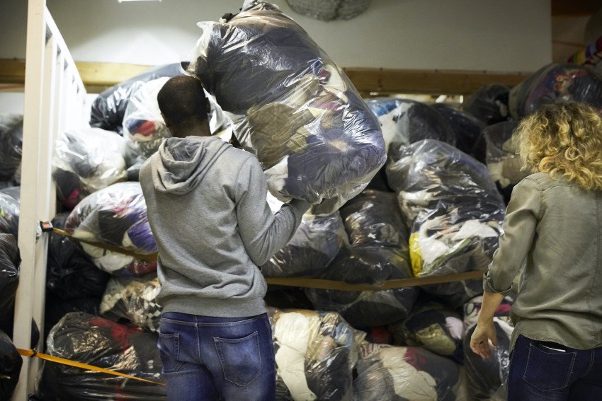 A man loads a bag of clothes onto a shelf of donations.