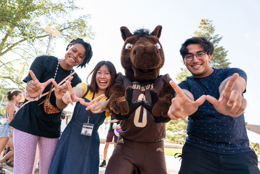 Students making a W with their hands smiling next to Buster Bronco.