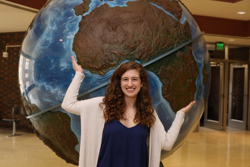 A student standing in front of a large globe sculpture.