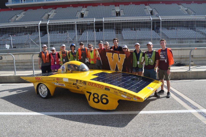 Photo of the 2019 WMU Sunseeker team standing in front of its solar race car on a track.