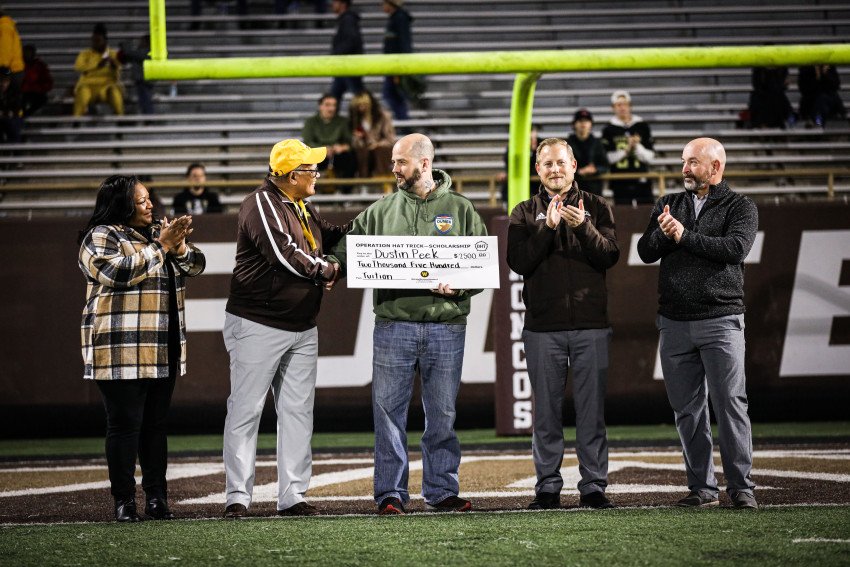 Dr. Deveta Gardner, President Edward Montgomery, Nick Collins, Dan Bartholomae and Kenneth Franks on the field at Waldo Stadium as Collins holds a large check for $2,500.
