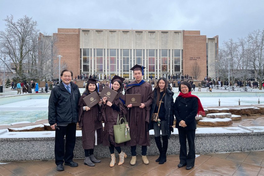 Three MBA graduates from Taiwan stand with Dr. Tarn at Fountain Plaza holding their degrees after the fall 2021 commencement ceremony. 
