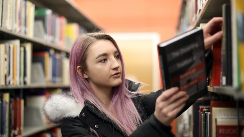Photo of girl pulling a book off the shelf in the library