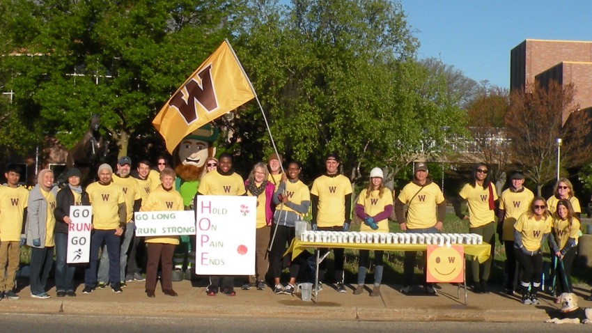 Volunteers pose with a WMU flag at a Kalamazoo Marathon Excitement Zone on campus.