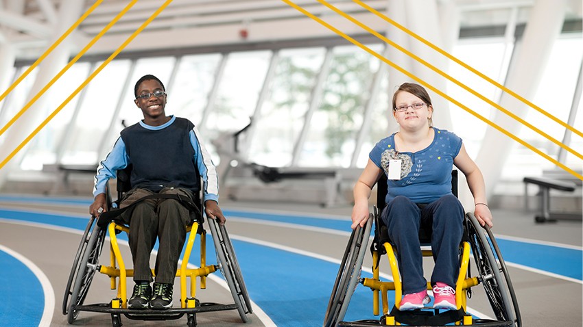Two disabled youth in wheelchairs push themselves around an indoor track.