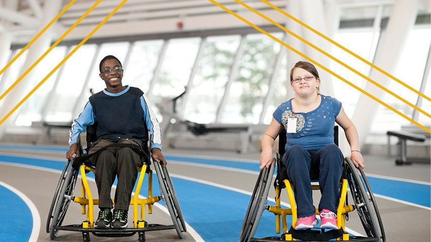 Two disabled youth in wheelchairs push themselves around an indoor track.