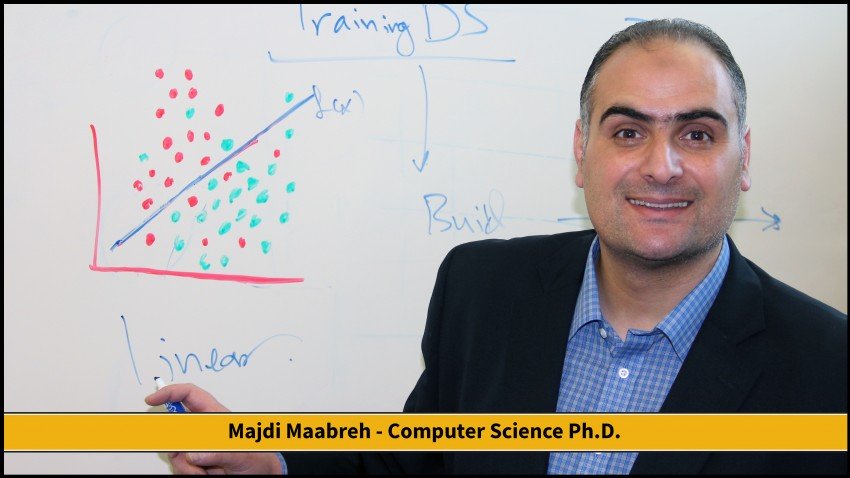 This photo shows Dr. Maabreth standing in front of a whiteboard in the front of a classroom. He is smiling and holding a marker pointing out the word Linear. On eat whiteboard is a coordinate graph plotting a large number of red and green dots that represent values for two different categories. There is a blue line that runs at about a forty-five degree angle from the center bisecting the upper right quadrant and the red dots are mostly above the line whereas the green dots fall primarily below the line. We are unable to see what the dots represent in this photograph as the legend for the graph is behind Dr. Maabreth. 